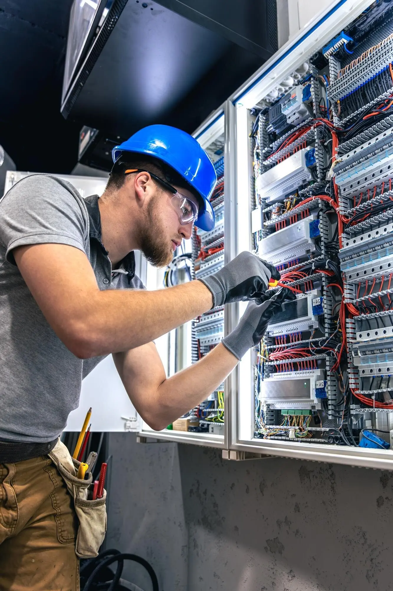 Мужчина-электрик в спецодежде работает у электрического щита.