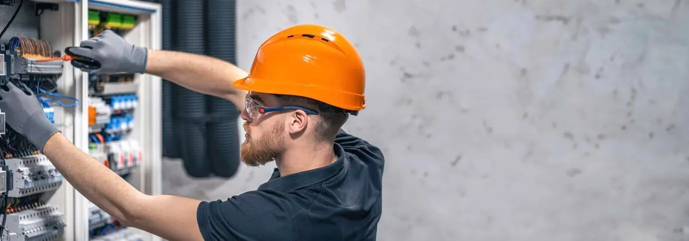 Электрик работает в распределительном щите с соединительным электрическим кабелем, есть свободное пространство для текста.